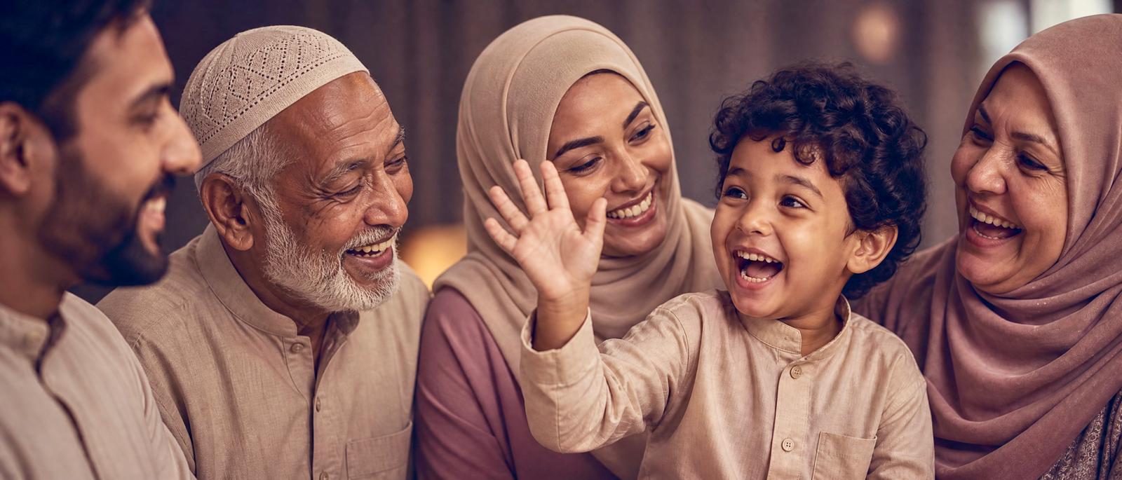Three generations of a family laughing together at home, a young child waving with his hand raised.